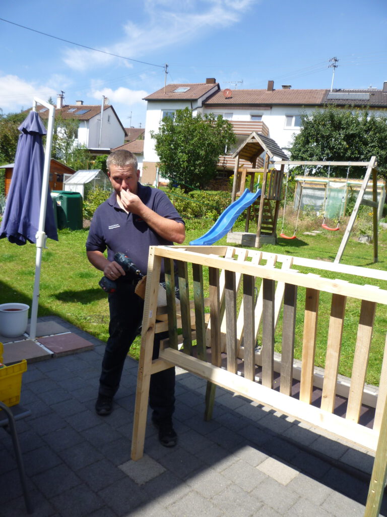 In einem Garten in einer Wohngegend mit Schaukel im Hintergrund wird eine Heuraufe selbst gebaut.