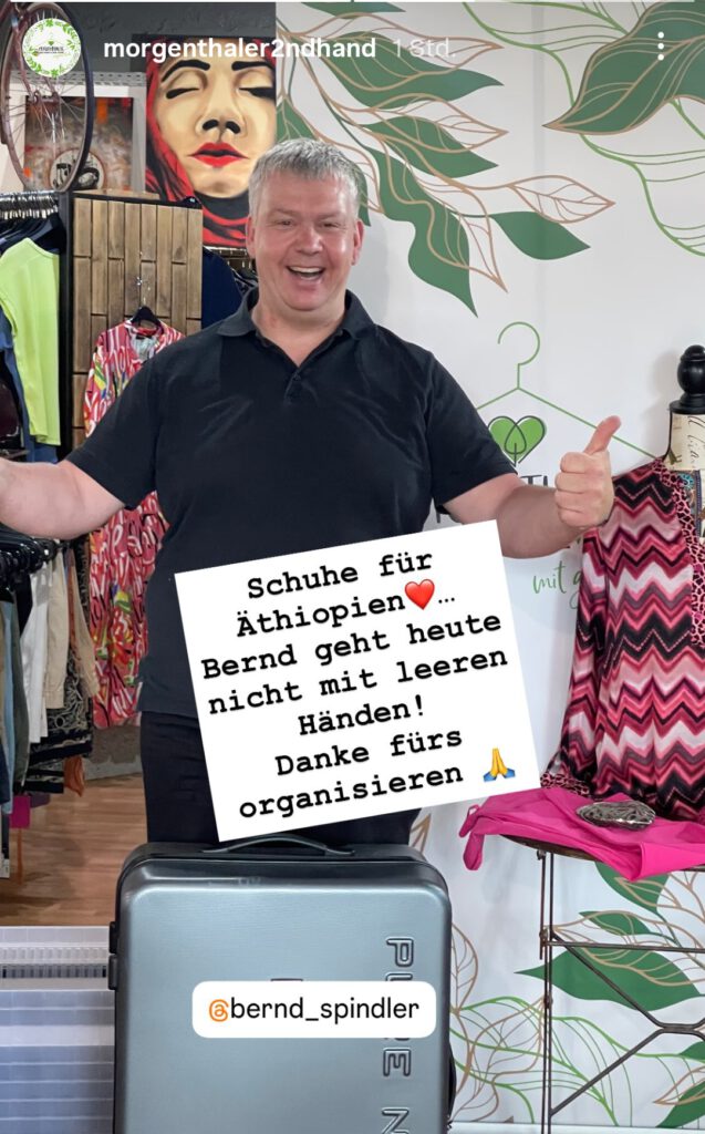 Bernd Spindler steht mit einem Koffer voller Schuhe im Morgenthalers Second Hand Laden und zeigt beide Daumen hoch – auf dem Schild steht „Bernd geht heute nicht mit leeren Händen!“