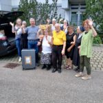 Gruppenbild der Helferinnen und Helfer des Aktionstags Äthiopien 2025 in Schwäbisch Gmünd, die lachend und winkend neben Schuhspenden und einem Koffer stehen.