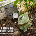 Froschfigur neben einer Gießkanne in einem Hochbeet mit Schafwolle als natürlichem Wasserspeicher gegen Trockenheit