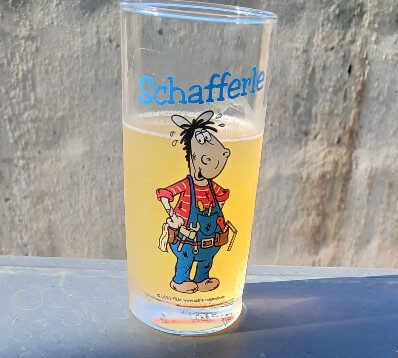 Ein Glas Apfelschorle im Schafferle-Glas auf einem Grill mit Thermometer an einem heißen Sommertag – erfrischend mit Bio-Apfelsaft von regionalen Streuobstwiesen.