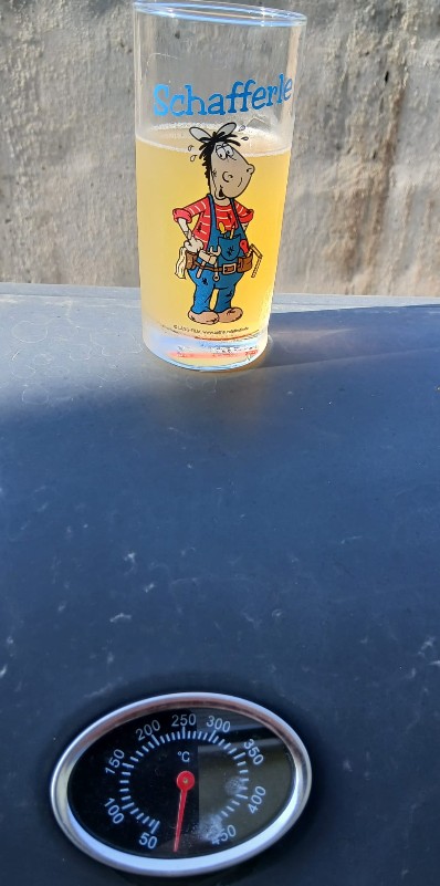 Ein Glas Apfelschorle im Schafferle-Glas auf einem Grill mit Thermometer an einem heißen Sommertag – erfrischend mit Bio-Apfelsaft von regionalen Streuobstwiesen.